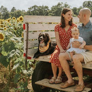 Family sitting on the wagon with a dog and sunflowers in the background.