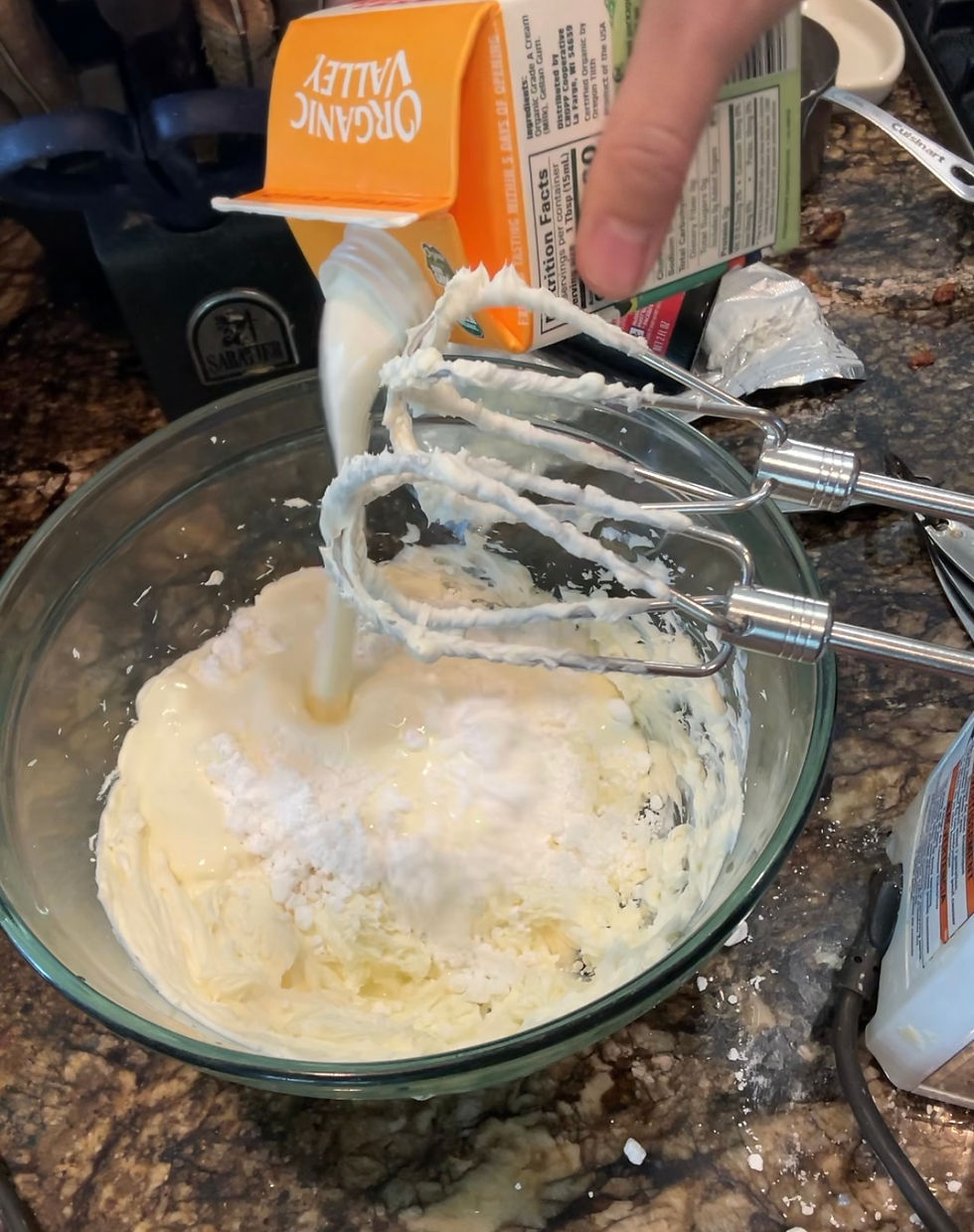 Milk is being poured from an orange carton labeled "Organic Valley" into a mixing bowl with batter, on a granite countertop.