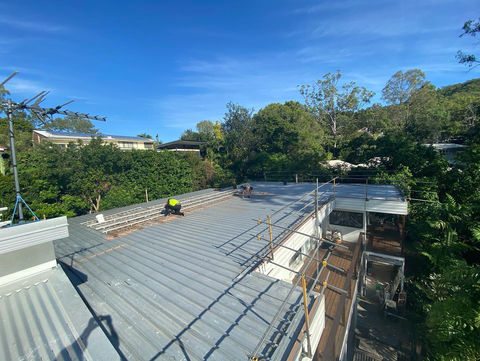Roof repairs with workers on a rooftop under a blue sky, roof repair gold coast