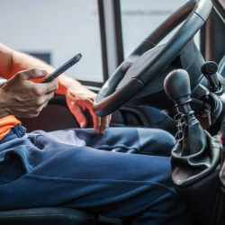 Truck driver sitting in the cab using a mobile phone for load updates and workflow management, illustrating the importance of native mobile apps in modern Transportation Management Systems like Amous TMS