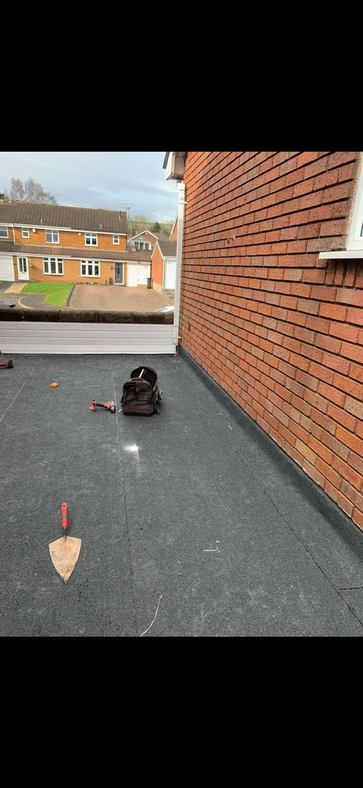Newly fitted felt flat roof with tools beside brick wall junction