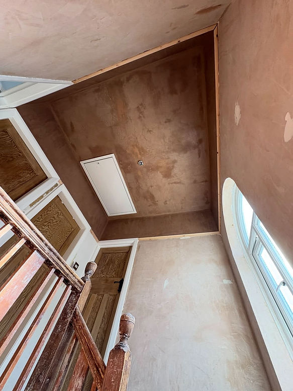 Stairwell with rough plastered walls, wooden doors and a loft hatch awaiting plastering