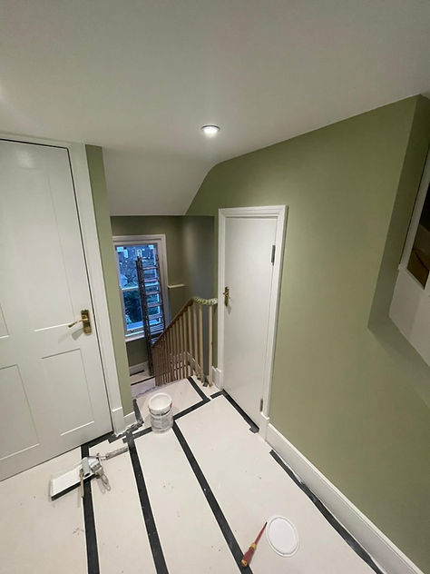 Freshly painted sage green hallway walls with white doors skirting boards and floor protection sheet during refurbishment