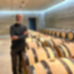 Winemaker standing among oak barrels in a Tuscia winery cellar in Caprarola, surrounded by rows of ageing wine casks.