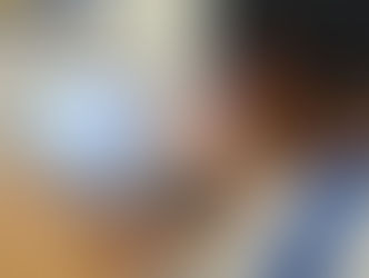 Suhani in white and blue shirt types on a laptop at a wooden desk. Posters are on the wall, and a purple bottle sits nearby.