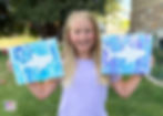 Girl holding up shark paintings.