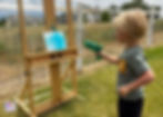 Boy using a water gun to squirt paint onto canvas.
