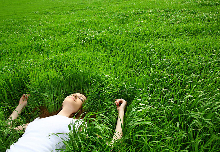 Woman lying in tall green grass with her eyes closed, smiling.