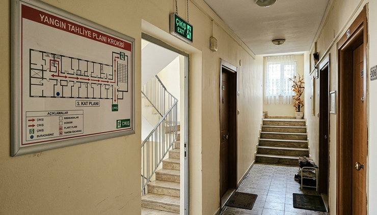 Geniş açı görünümde apartman koridorunda duvara asılmış tahliye krokisi bulunuyor.
