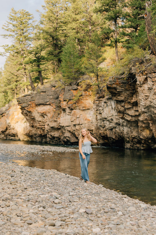 Senior girl standing in a green meadow surrounded by pine trees in Wyoming