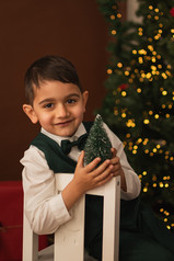 A boy with a toy Christmas tree sitting in front of the twinkle lights