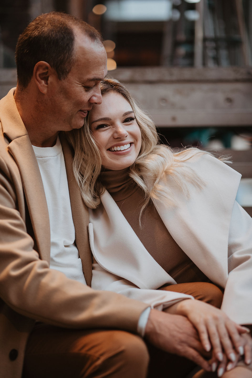 Couple smiling together on city steps during a warm and romantic winter photoshoot in Sydney CBD.