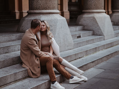 Couple sitting on sandstone steps during a winter couples photoshoot in Sydney CBD, wearing neutral coats and sharing a quiet romantic moment.