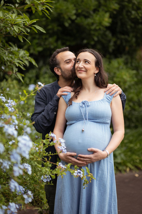 Pregnant couple in a blue dress surrounded by blue flowers - maternity photoshoot by Family Stories Photography