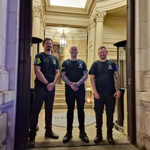 Three security guards standing in the doorway of a grand stone building