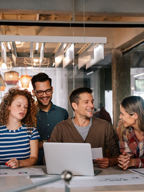 Grupo de personas sentadas alrededor de una mesa con una laptop, colaborando en una agencia de publicidad en Guatemala.
