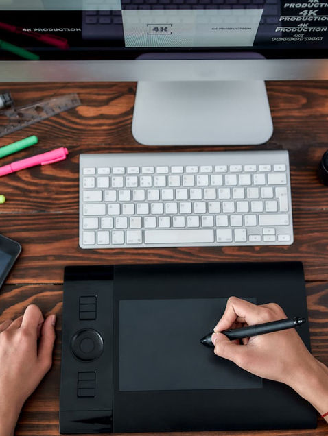 Persona trabajando en una computadora con una tableta y otros objetos, en un entorno de agencia de publicidad en Guatemala.