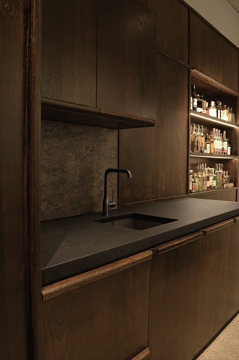 Office kitchenette and bar area with textured cabinetry, leathered granite counter and cork splashback in boutique workspace.