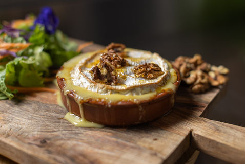 Camembert rôti aux noix avec salade verte sur planche en bois.
