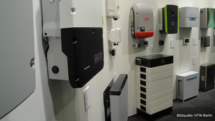 Verschiedene Batteriespeicher in einem Ausstellungsraum, unterschiedlich groß und farbig, an einer weißen Wand montiert.
