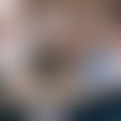 Three people are at a car dealership, engaged in discussion around a desk. A computer screen and car wheel displays are visible in the background.