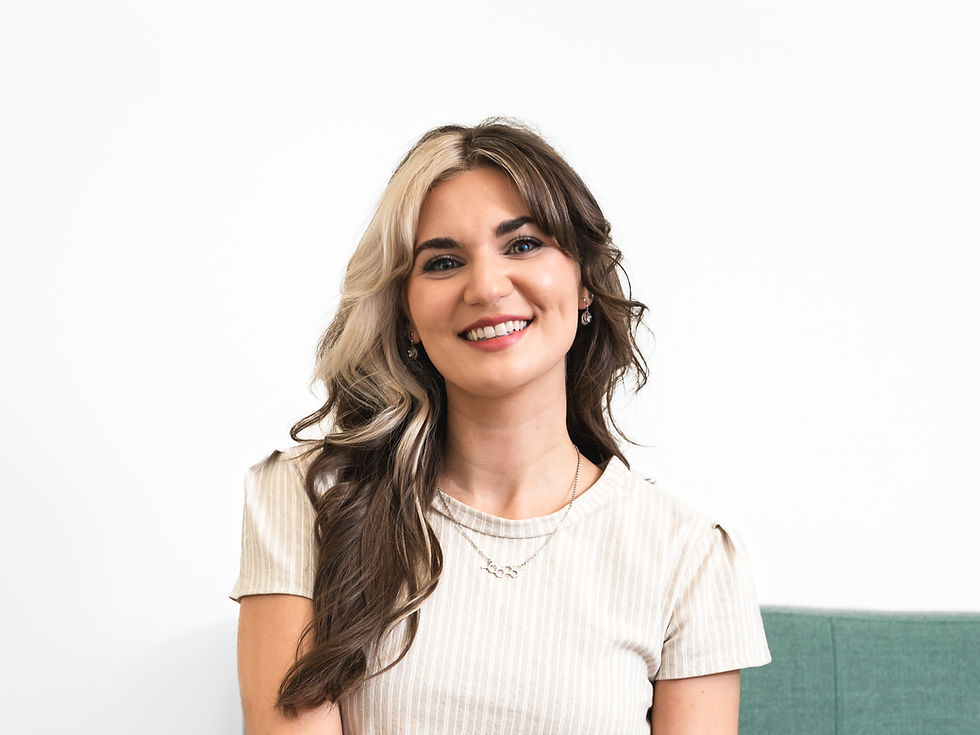 Smiling woman with two-tone wavy hair in a white striped top, seated against a plain white background with a teal sofa edge.