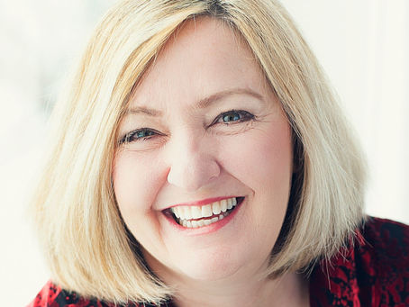 Smiling woman with blonde hair in a red patterned top; bright, soft-focus background. Mood is cheerful and inviting.