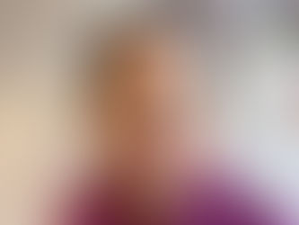 Woman smiling in a room with abstract art on the white wall. She wears a magenta scarf, creating a warm and creative atmosphere.