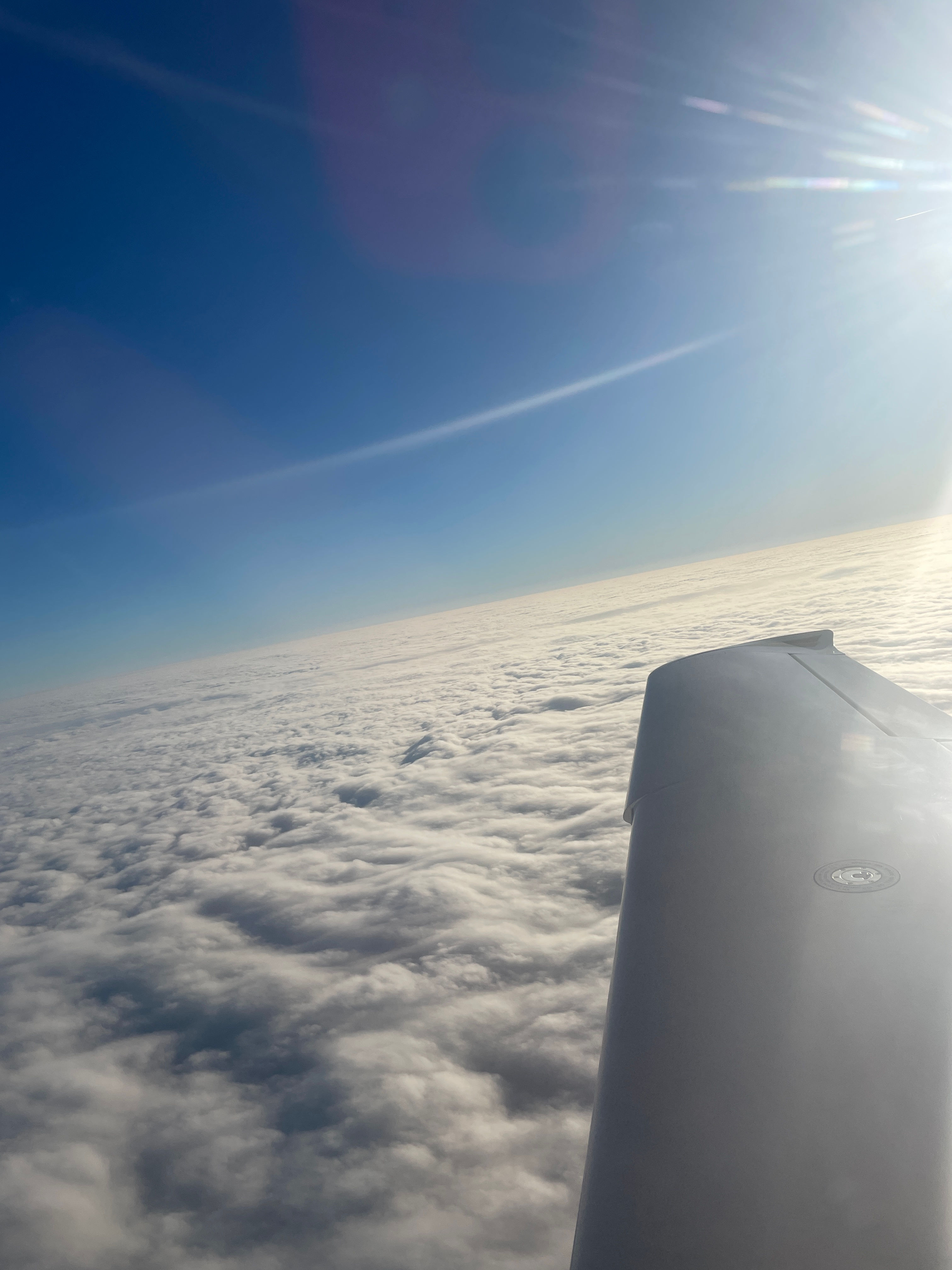 Aircraft wing above clouds, bright blue sky