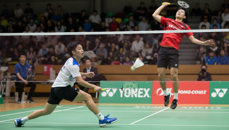 Eye-level view of two badminton players during a fast rally.