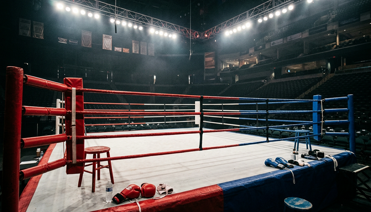 Wide-angle view of a boxing ring under bright arena lights before a title fight.
