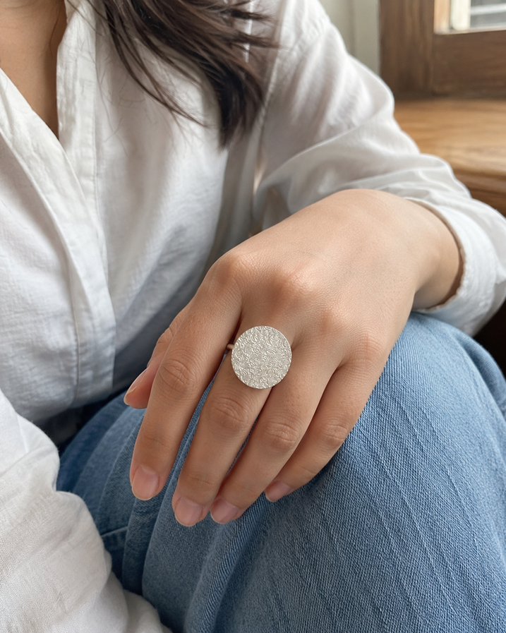 Textured silver-tone disc detail of brass ring