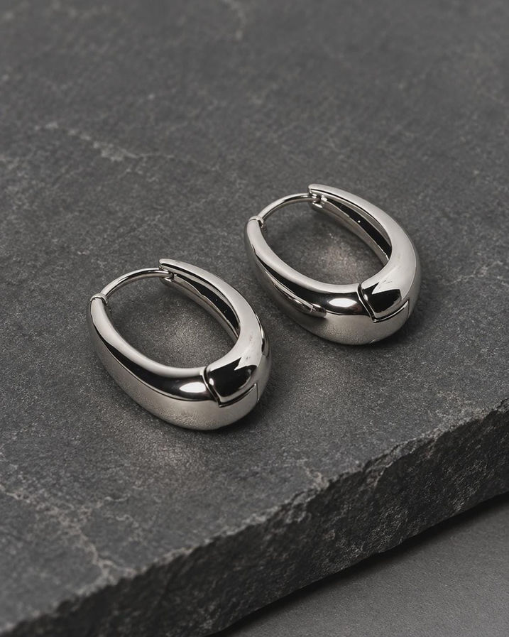 Silver plated chunky hoop earrings on dark slate, close up of oval huggie hoop