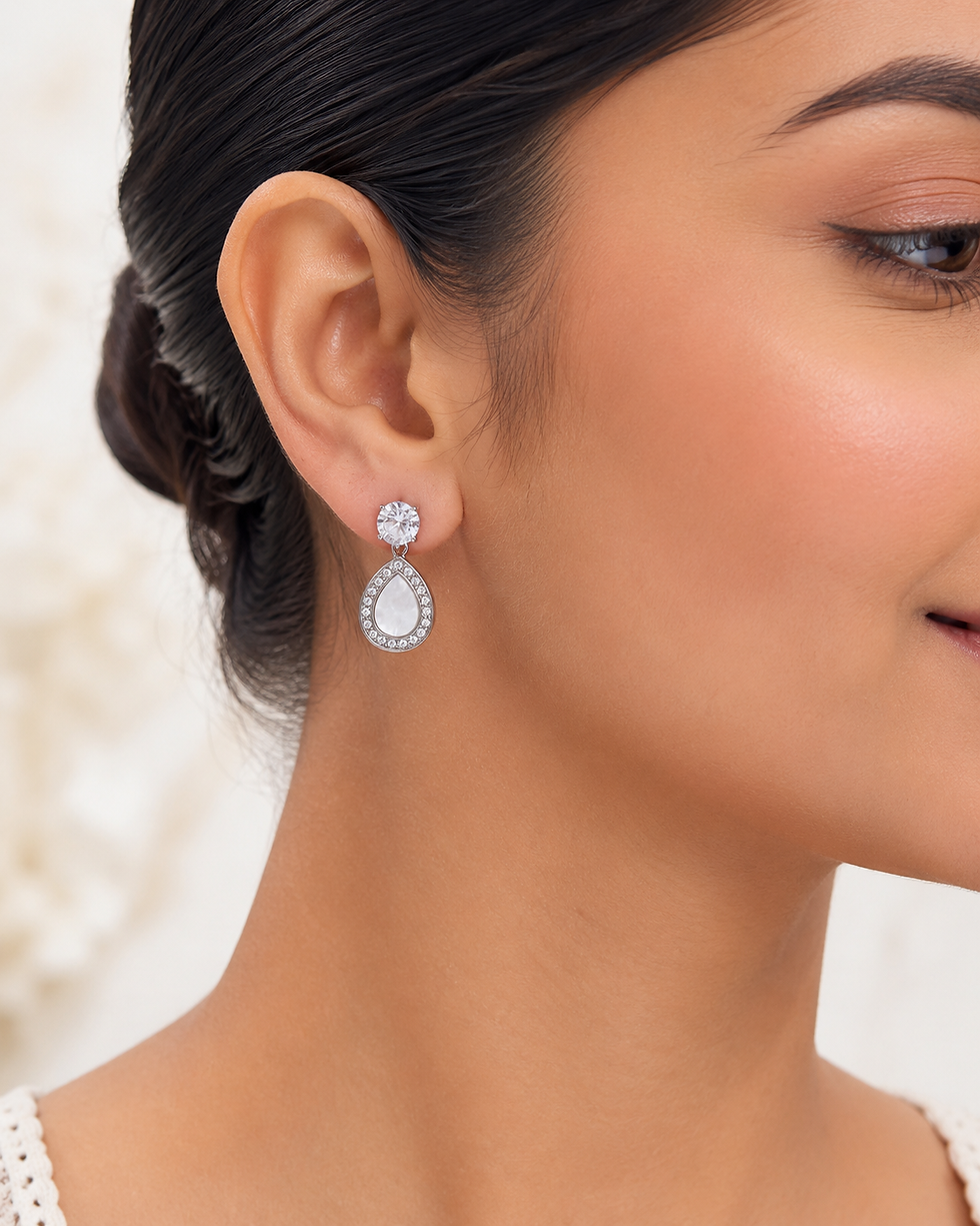 Model wearing silver pear stud-drop earrings with crystal-style top and white pearl-look centre.