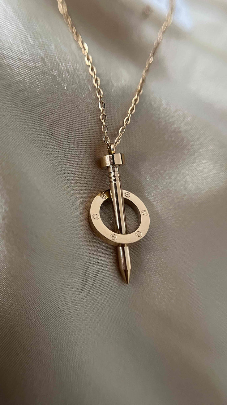 A trendy 18k gold-plated necklace with a nail pendant wrapped by a hoop, blending unconventional design with classic elegance