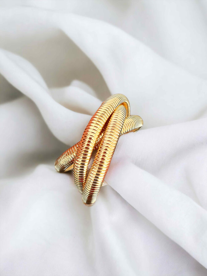 Gold coil bracelet with intertwined triple band design on white fabric