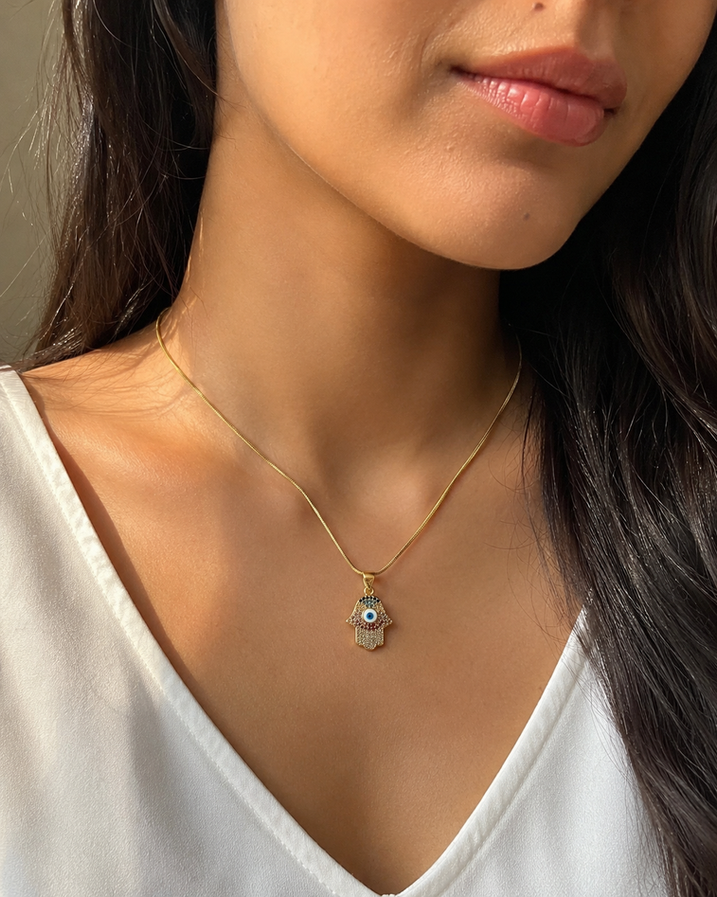 Indian model wearing a small Hamsa evil eye crystal pendant necklace with a gold-tone snake chain