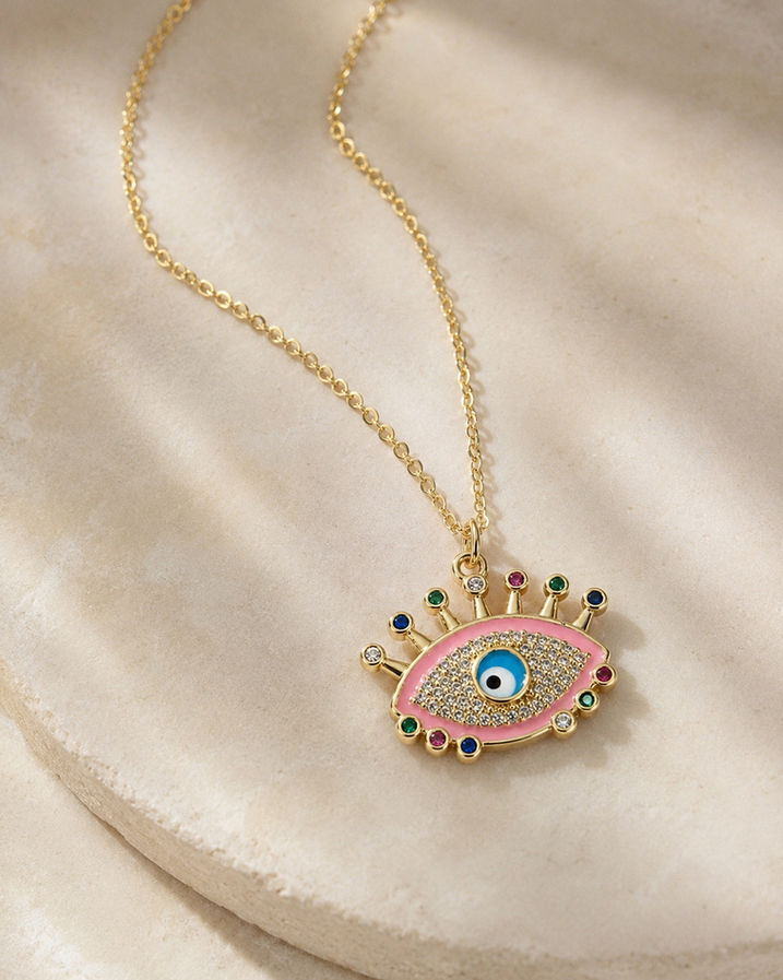 Pink crystal evil eye pendant necklace laid on a cream textured surface