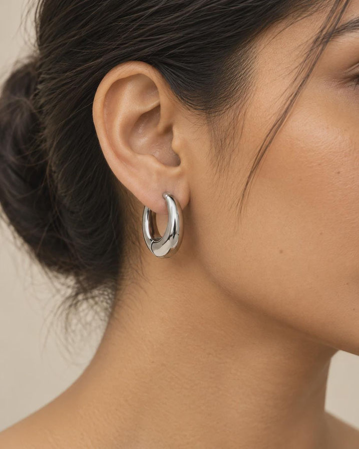 Model wearing silver chunky hoop earrings, everyday oval huggie hoops on ear