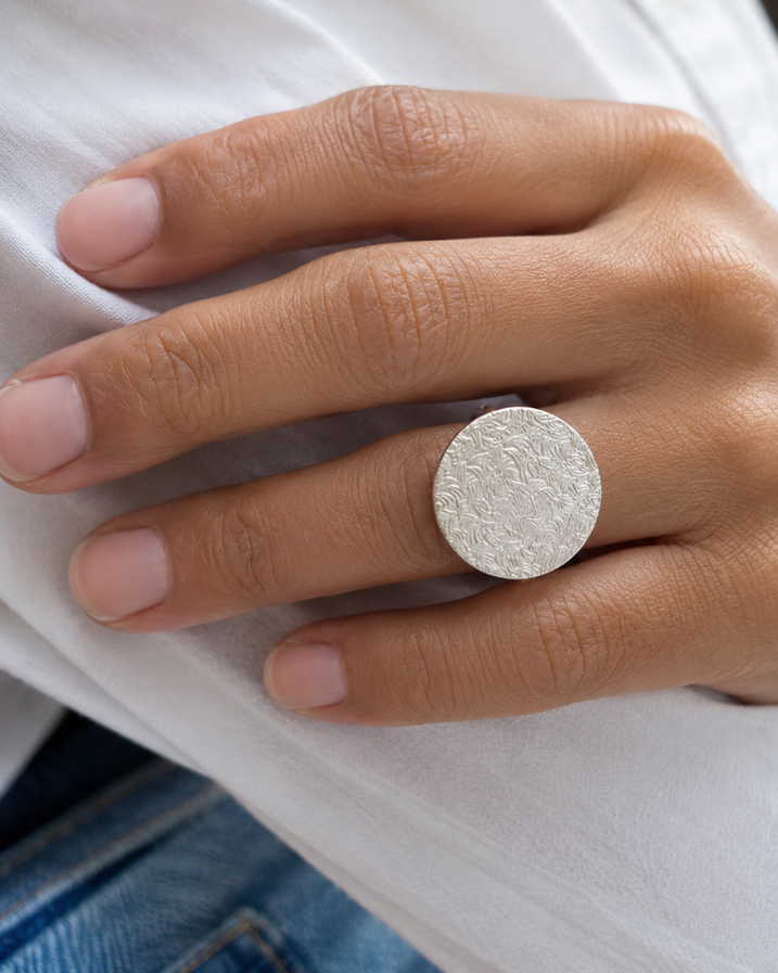 Close-up of textured silver disc on silver brass ring
