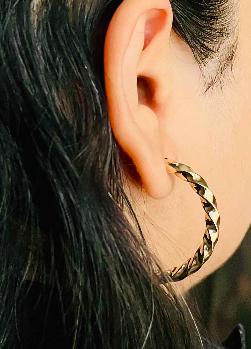 Gold twisted hoop earrings lying on a white surface, showcasing a sophisticated spiral design suitable for daily wear office