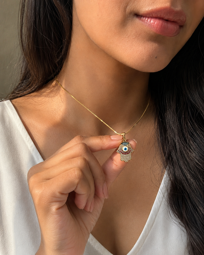 Close-up of a gold-tone Hamsa hand necklace with a blue evil eye on an Indian woman