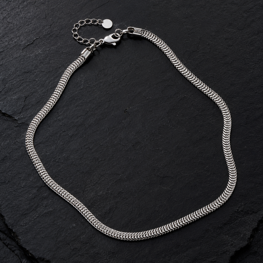 Stainless steel scale-link chain necklace displayed on a black textured surface