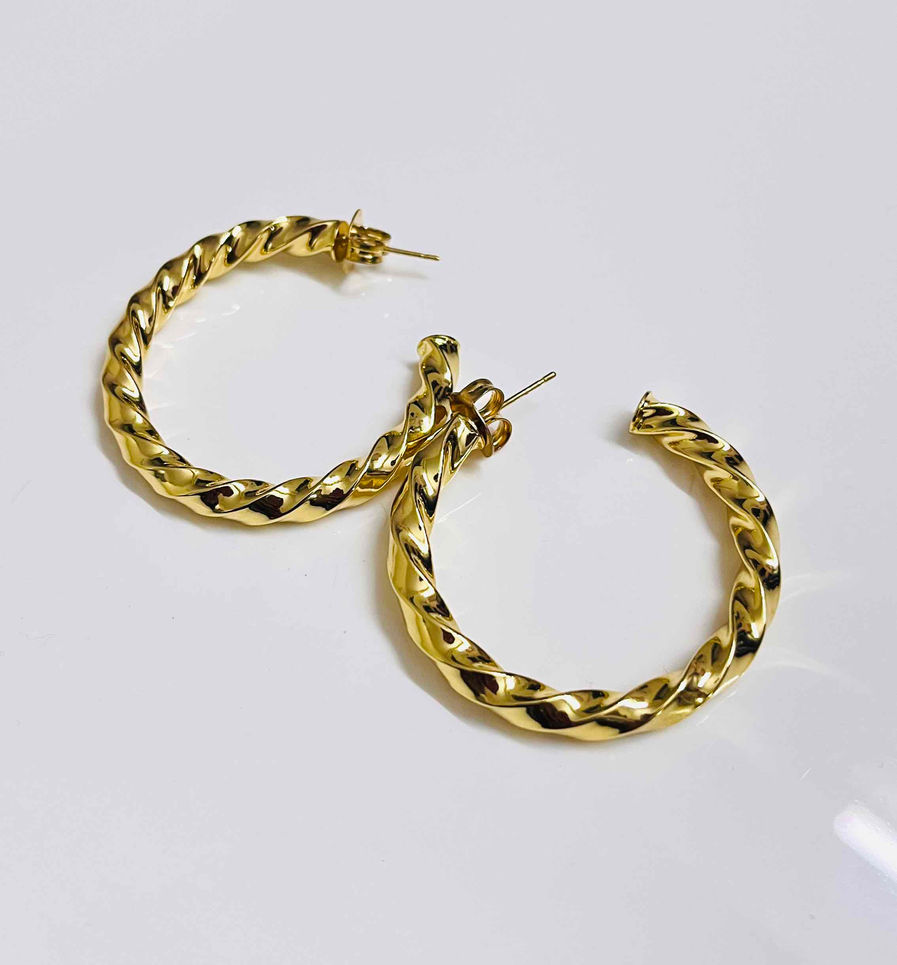 Gold twisted hoop earrings lying on a white surface, showcasing a sophisticated spiral design suitable for daily wear office