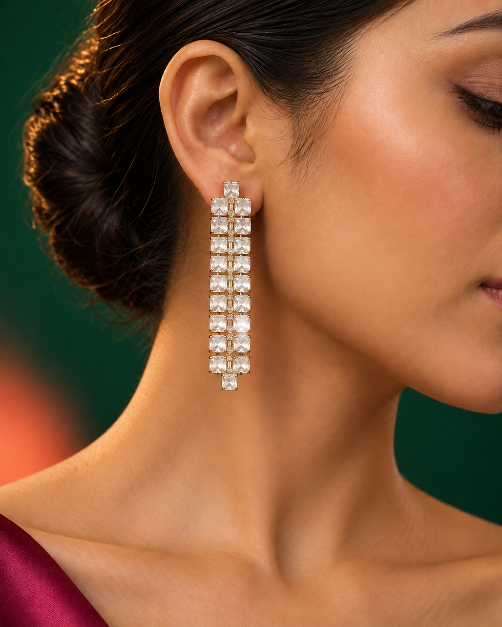Clear square-glass long drop earrings in gold-tone settings on a pink fabric background.
