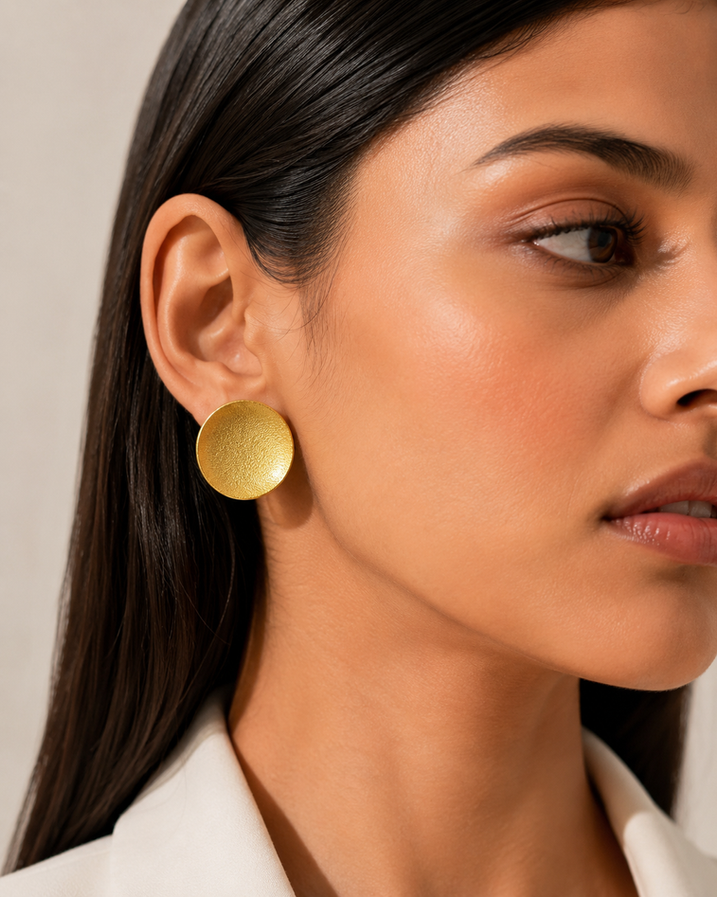Model wearing gold brass round statement earrings with white blazer