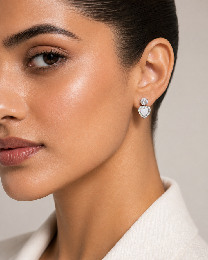 Silver heart stud earrings with sparkling crystal tops, rhinestone heart borders, and white pearl-style heart centers.