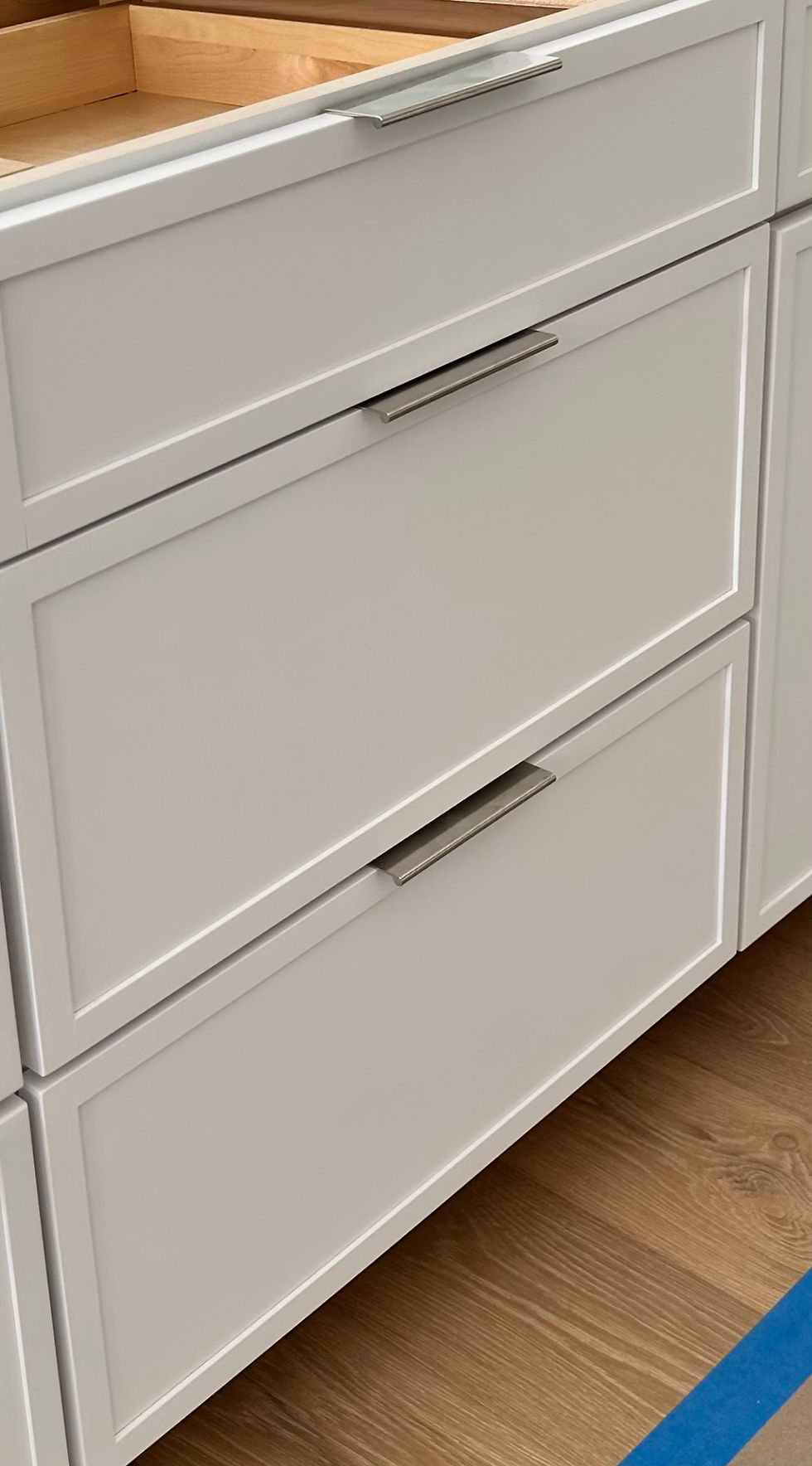 White moder/contemporary kitchen cabinets with chrome/silver handles/edge pulls for Modern and minimalistic look. sleek. Light wood floor.