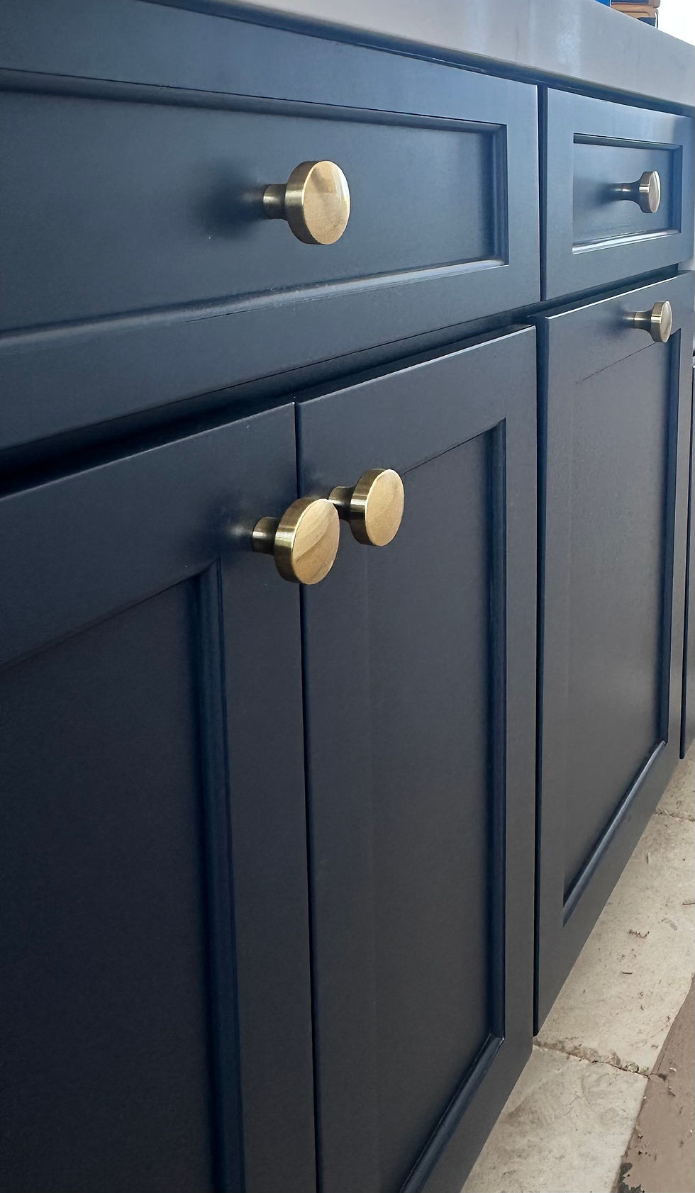 Dark blue kitchen cabinets with gold knobs, set against a tiled floor. The elegant design gives a modern, chic feel to the space.