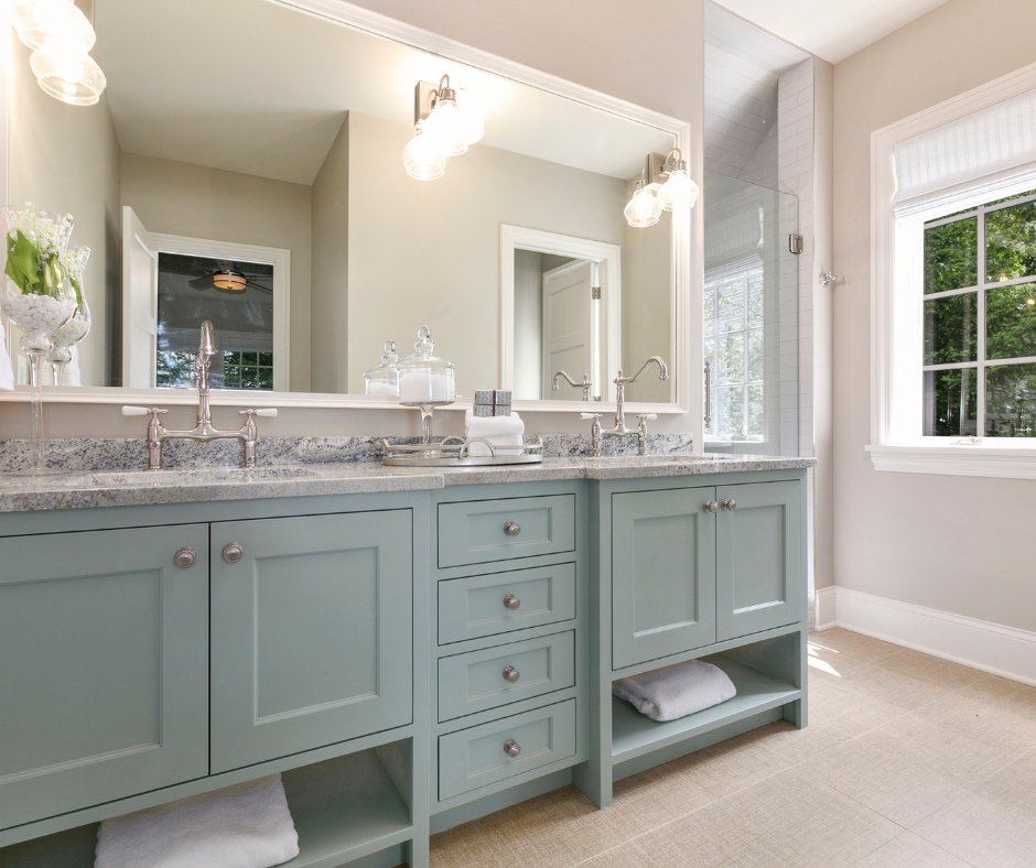 Modern bathroom with light blue double vanity, granite countertop, large mirror, and glass shower. Sunlight filters through a window. Relaxing mood.
